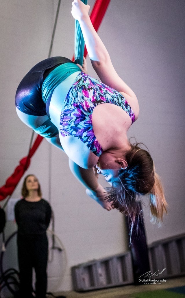 Luca, a white trans man, performs for the first time. He is suspended in the air, wrapped in fabric that hangs in a loop from the ceiling.